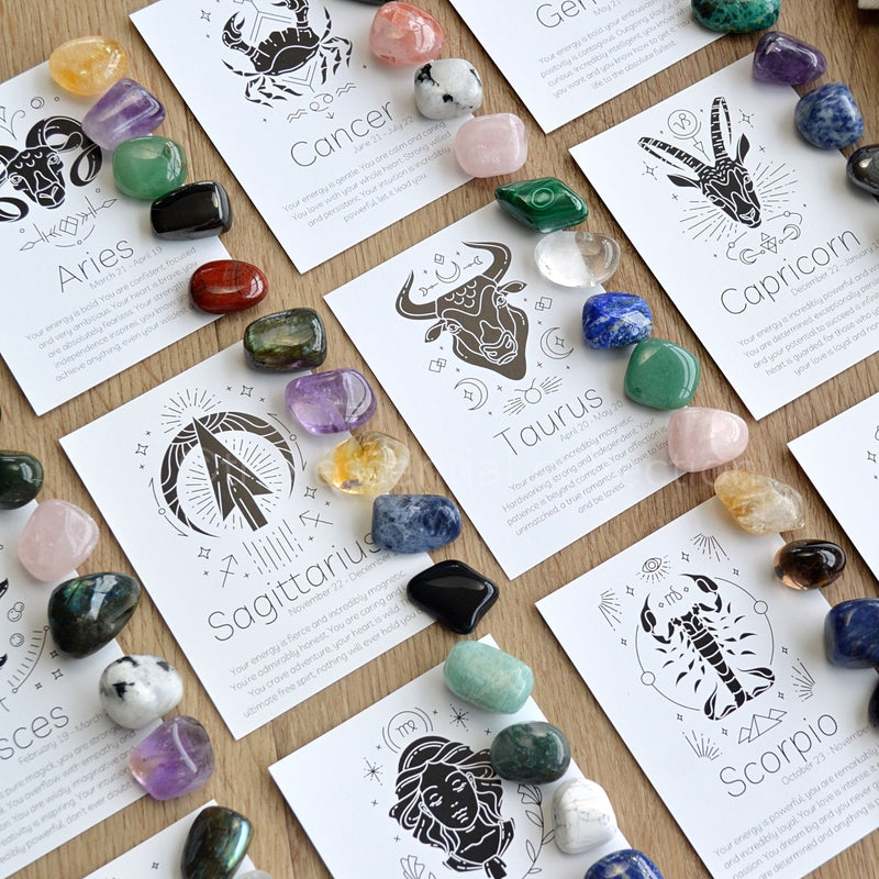 A flat lay of black and white printed cards with writing about each zodiac sign, next to each card is five crystals associated with that particaular zodiac sign. 