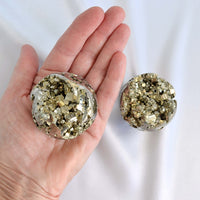 Two crystal balls with pyrite crystals held in a hand against a white background