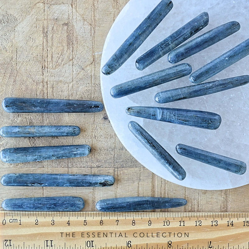 blue kyanite tumbled blades on a round selenite plate next wood ruler.